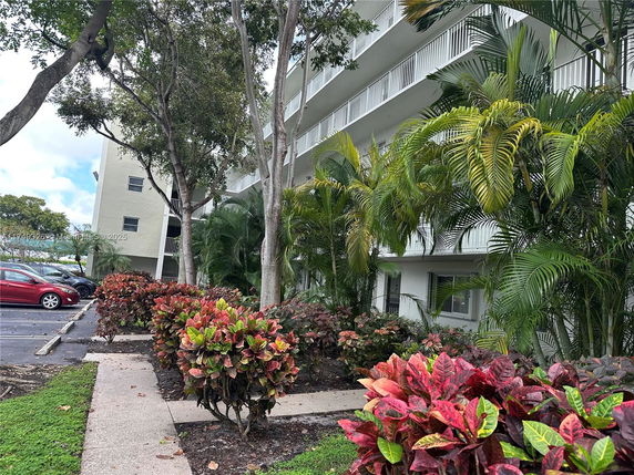 View of a multi-story building with surrounding plants and parking area.