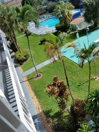 View of landscaped area with palm trees and a swimming pool from a building.
