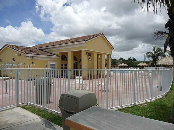View of a clubhouse with a swimming pool area enclosed by a fence.