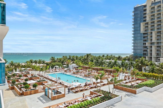 View of luxurious beachfront pool area surrounded by palm trees and modern buildings.