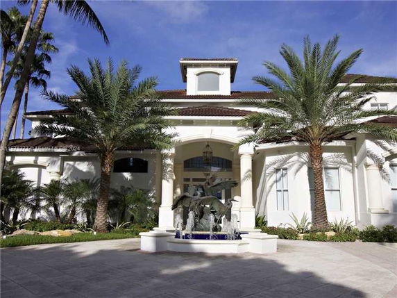 Front view of a two-story house with palm trees and a decorative fountain.