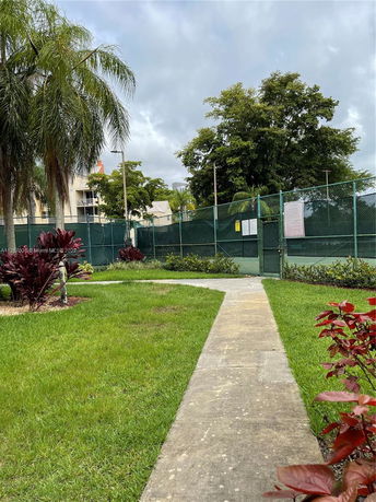 View of an outdoor tennis court surrounded by greenery and a fence.