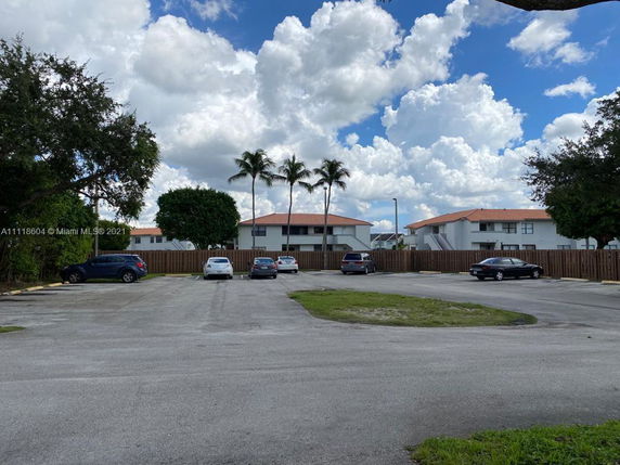 Outdoor parking area with several parked cars in front of residential buildings with red roofs.
