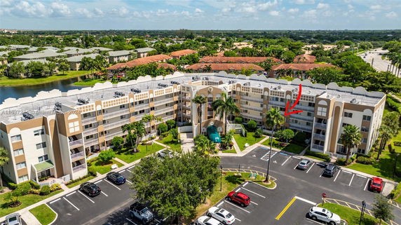 Aerial view of a multi-story apartment complex with landscaped surroundings and parking area.