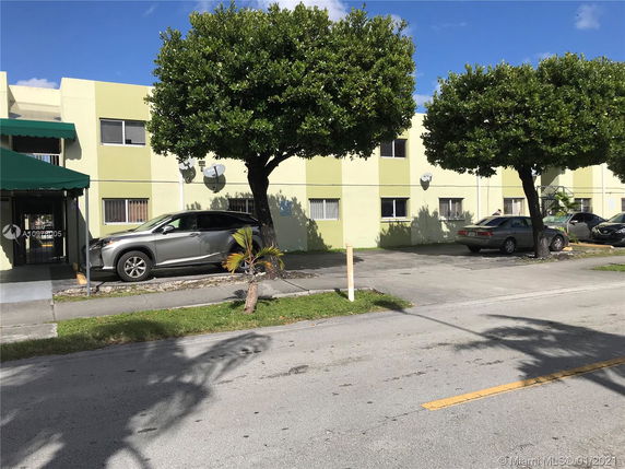 Front view of a multi-story building with parking spaces and green awnings.