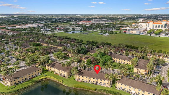 Aerial view of a residential area with multiple buildings, parking areas, and greenery, set against a distant urban backdrop.
