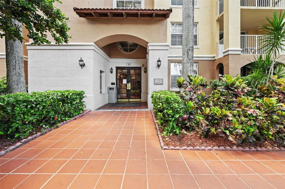 Front view of a multi-story building entrance with archway and decorative plants.