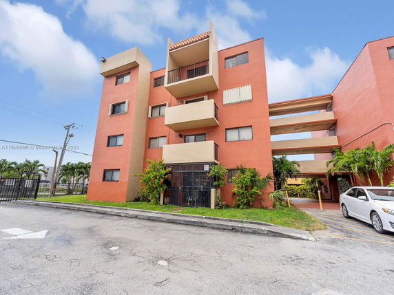 Front view of a multi-story residential building with balconies and a parking area.