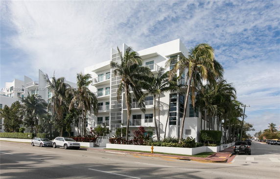 Front view of a multi-story residential building with balconies and palm trees.