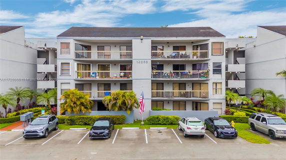 Front view of a multi-story residential building with balconies and parked cars.