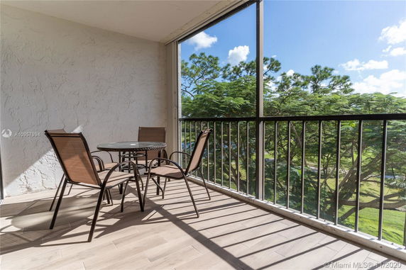 Balcony with a table and chairs overlooking a view of trees and clear skies.