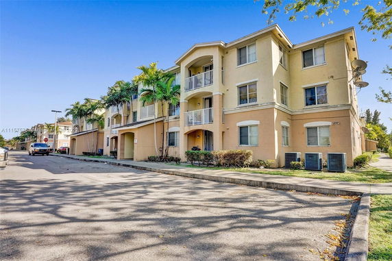 Front view of a three-story apartment building with balconies and outdoor parking.