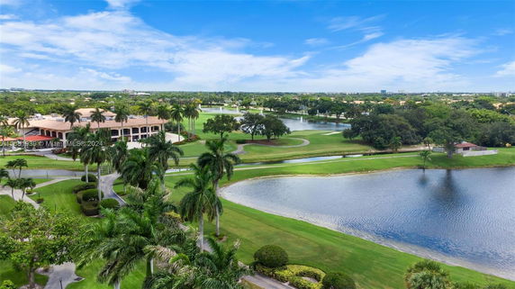 View overlooking a large building surrounded by palm trees and extensive greenery, with a lake in the foreground.