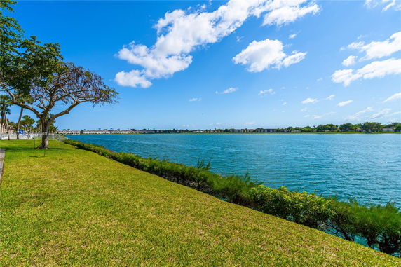 Scenic view of a lakeside area with grassy land and trees under a blue sky.