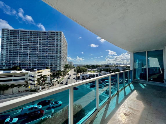 Panoramic city view from a balcony with glass railing and adjacent high-rise building.