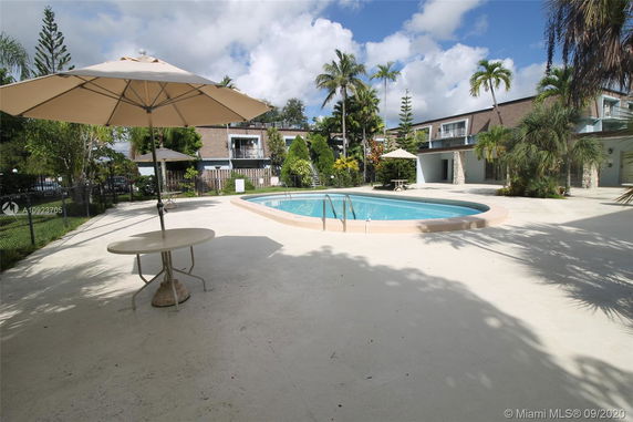 Outdoor swimming pool area with umbrella and table surrounded by residential buildings.