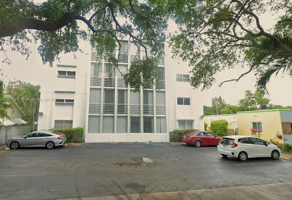 Front view of a multi-story building with large windows and adjacent parking area.