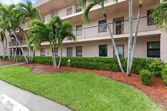 Front view of a multi-story building with balconies and a landscaped area with palm trees.