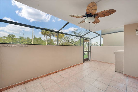 Enclosed outdoor patio area with a ceiling fan and tiled floor, providing a view of the surrounding trees and sky.