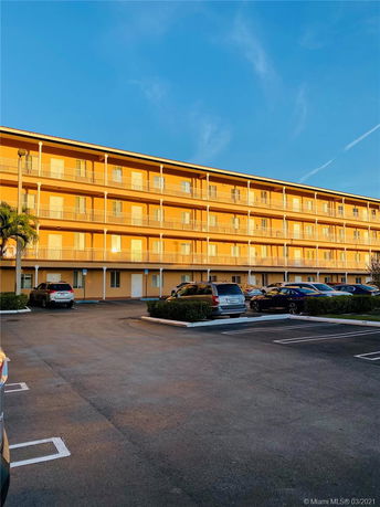 View of a multi-story building with a parking area in front.