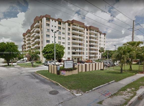 Front view of a multi-story condominium building with multiple balconies and parking lot.