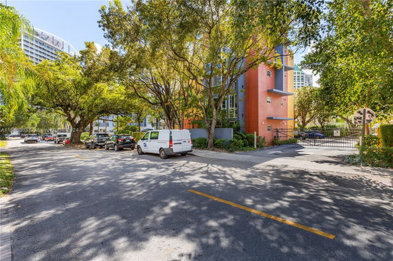 Street view with parked cars and trees, adjacent to a colorful building.