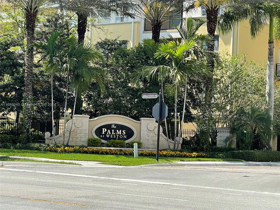 Front view of a building with a sign reading 'The Palms at Weston' surrounded by palm trees.