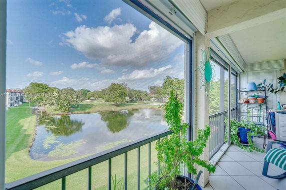 A balcony view overlooking a pond and greenery, with plants and railing in the foreground.