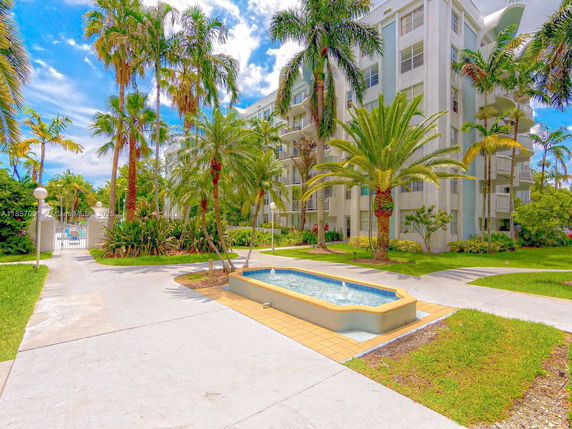 Front view of a multi-story residential building with a pathway and tropical landscaping.