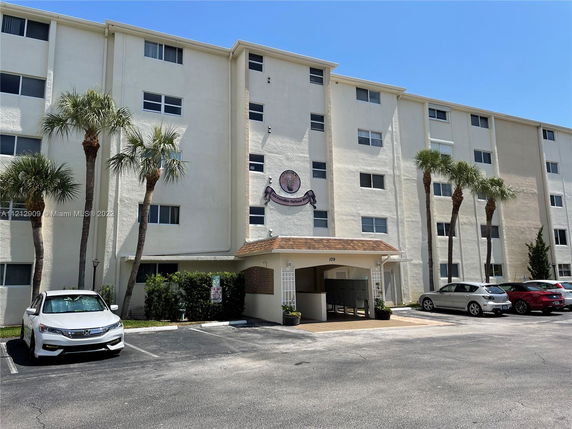 Front view of a multi-story residential building with a central entrance and surrounding parked cars.