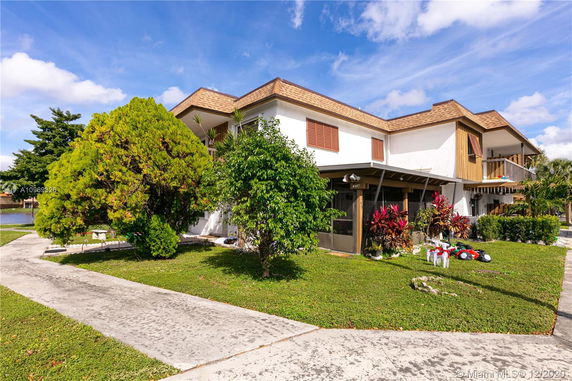 Front view of a two-story house with a flat roof and colorful plants in the garden.