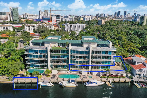 Aerial view of a multi-story waterfront building with several balconies and a small marina with boats docked.