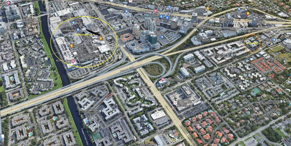 Wide aerial view of a city area with buildings, roads, and greenery.