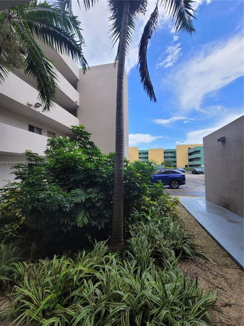 View of building exterior with plants and a parked car.