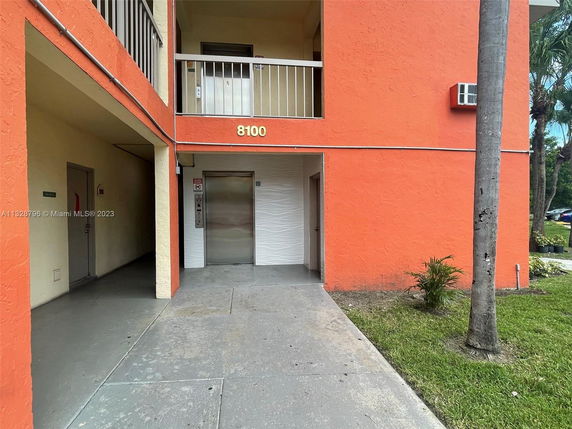 Front view of a multi-story building with an orange facade, balcony, and entrance with an elevator.