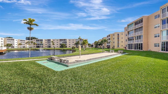 View of a large residential complex with multiple multi-story buildings surrounding a landscaped area with a small lake and walkway.