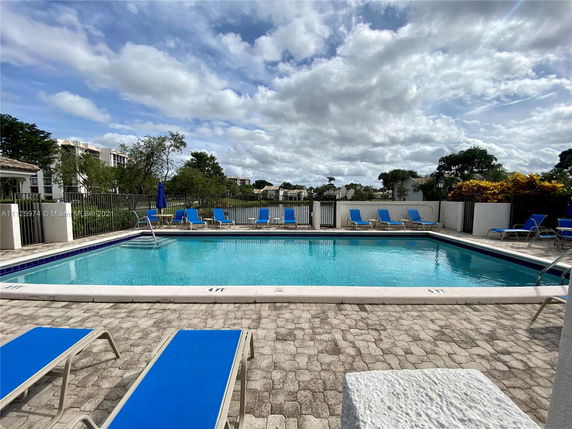 View of a swimming pool area with lounge chairs and surrounding apartment buildings.