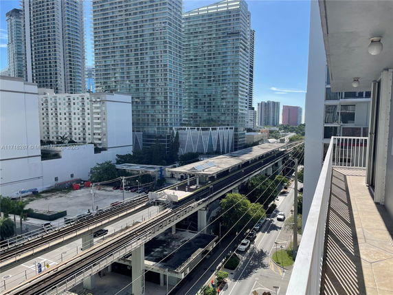 View from a building balcony overlooking other high-rise buildings and a transportation line in an urban area.