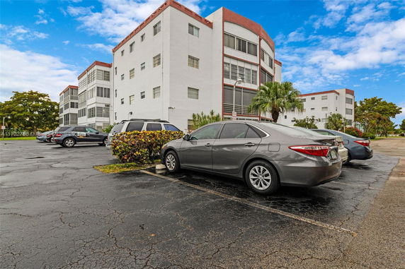 Outdoor parking area with cars in front of a multi-story building.