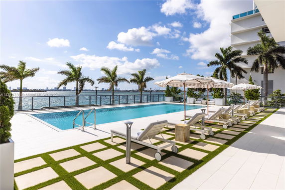 Outdoor swimming pool area with lounge chairs and umbrellas by the water.