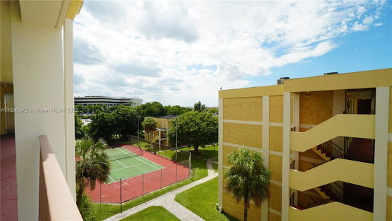 View of an outdoor tennis court next to a multi-story building.