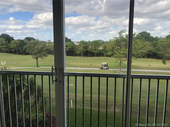 View from a balcony overlooking a grassy field with trees and a path where a golf cart is passing by.