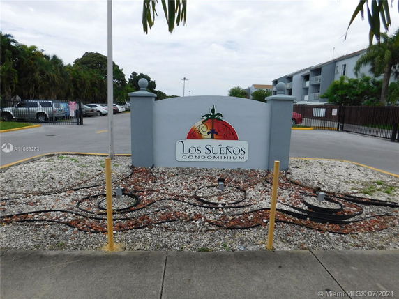 Entrance sign of Los Sueños Condominium with parking area in the background.