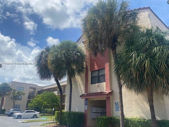Front view of a multi-story residential building with palm trees and parking area.