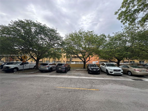 Outdoor parking area with multiple vehicles and surrounding trees.