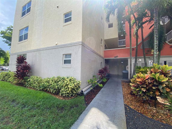 Front view of a multi-story building with a pathway surrounded by plants.