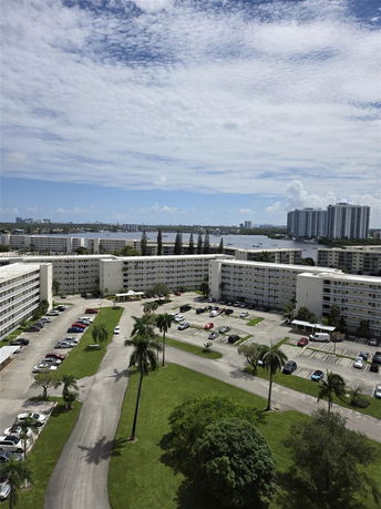 View overlooking several multi-story apartment buildings and a parking lot with water and high-rise buildings in the distance.