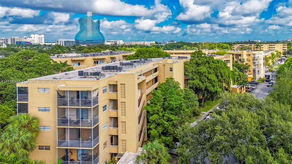 Aerial view of a multi-story beige apartment building with a guitar-shaped building in the distance.