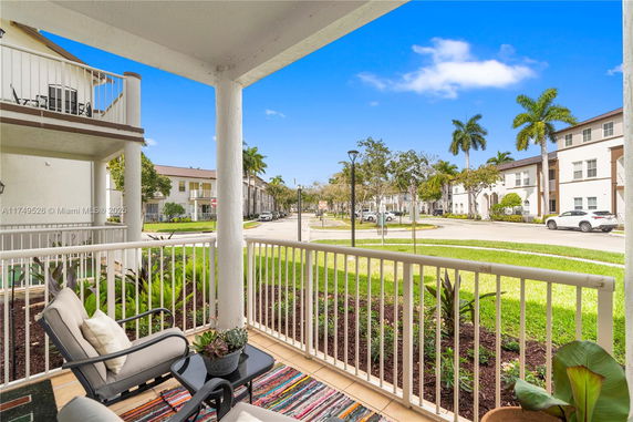 View from a covered porch overlooking a residential street with palm trees and apartment buildings.