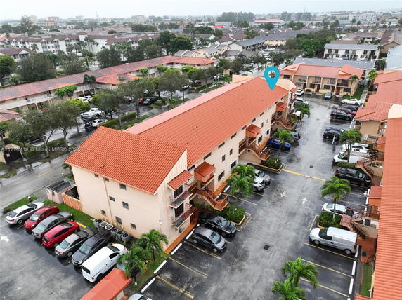 Aerial view of a multi-story residential building with an adjacent parking area and orange roof tiles.